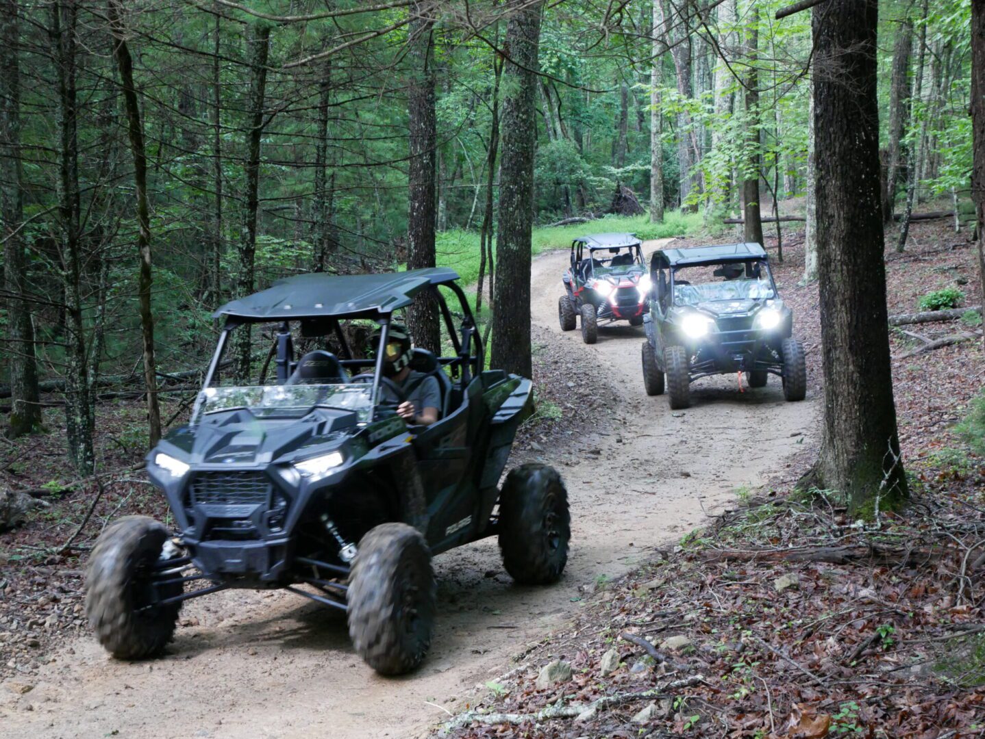 A group of people riding off road vehicles on dirt path.