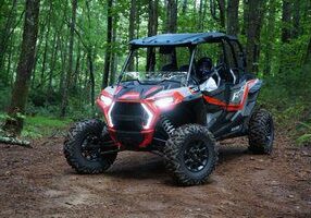 A red and black four wheeler parked in the woods.